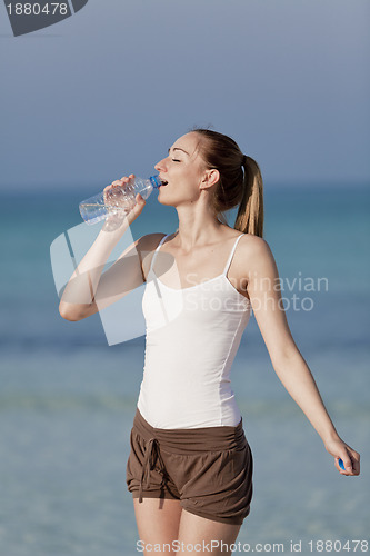 Image of Woman drinking water from a bottle on the beach portrait