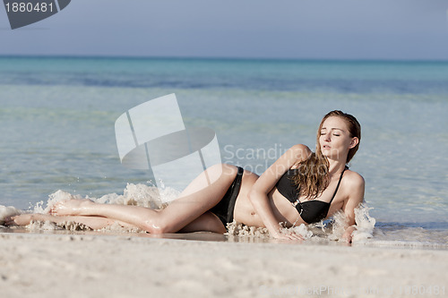 Image of Young woman in black bikini on the beach in the water landscape