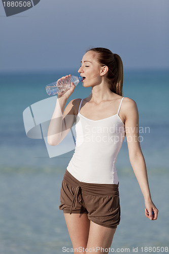 Image of Woman drinking water from a bottle on the beach portrait