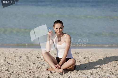 Image of Woman drinking water from a bottle on the beach landscape