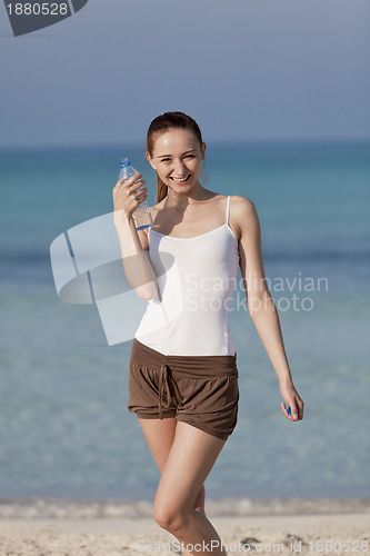 Image of Woman drinking water from a bottle on the beach portrait
