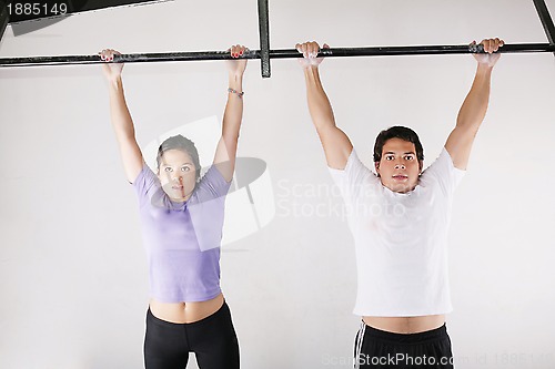 Image of Female and male bodybuilder doing pull-ups on metal bar on gym