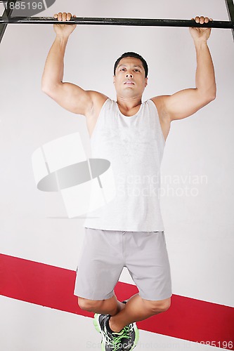 Image of Strong man doing pull ups on a bar in a gym in the background. 