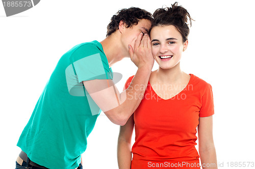 Image of Handsome boy talking secret to young girl in her ear