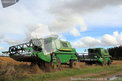 Image of Two green combine harvesters by wet field