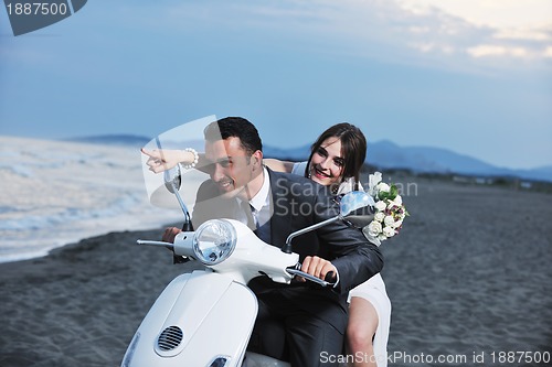 Image of just married couple on the beach ride white scooter