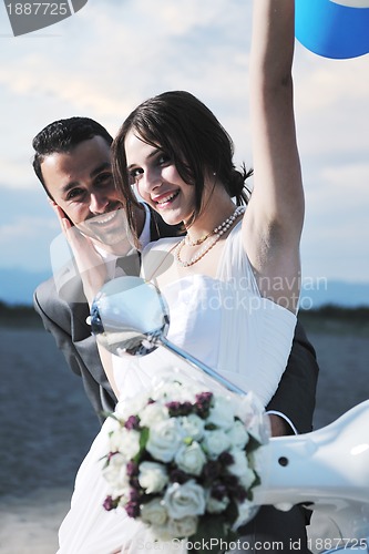 Image of just married couple on the beach ride white scooter