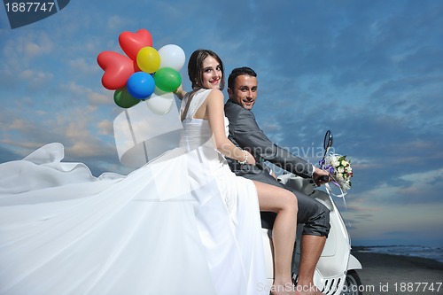 Image of just married couple on the beach ride white scooter