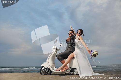 Image of just married couple on the beach ride white scooter