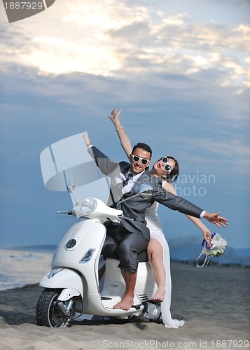 Image of just married couple on the beach ride white scooter