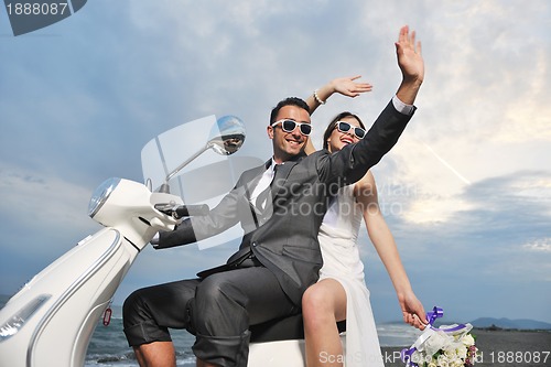 Image of just married couple on the beach ride white scooter