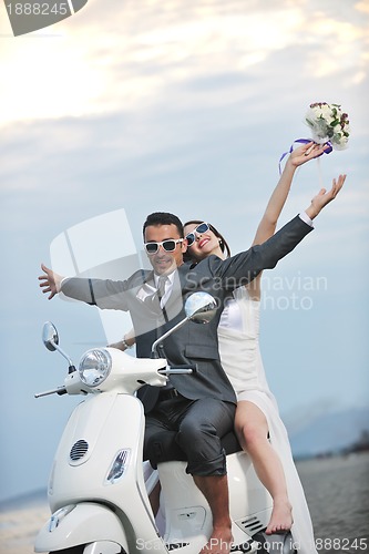 Image of just married couple on the beach ride white scooter
