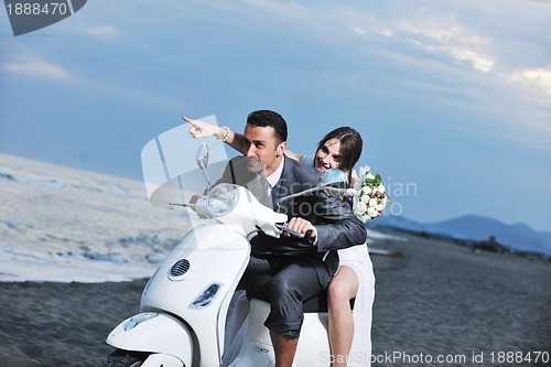 Image of just married couple on the beach ride white scooter