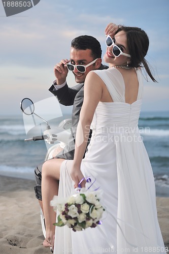 Image of just married couple on the beach ride white scooter