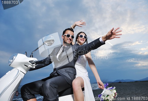 Image of just married couple on the beach ride white scooter