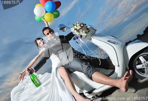 Image of just married couple on the beach ride white scooter