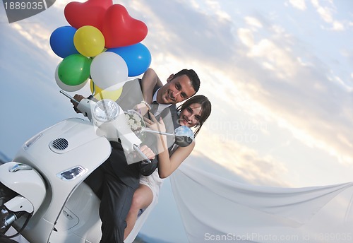 Image of just married couple on the beach ride white scooter