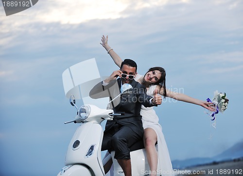 Image of just married couple on the beach ride white scooter