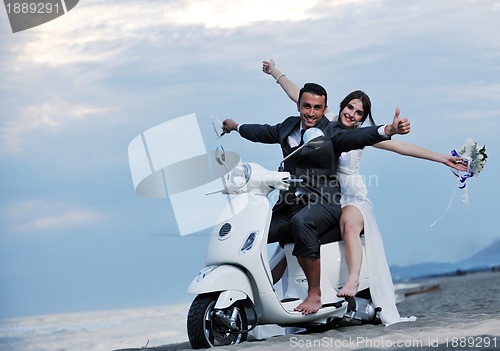 Image of just married couple on the beach ride white scooter