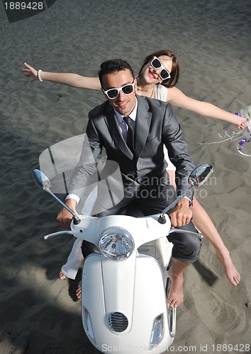 Image of just married couple on the beach ride white scooter