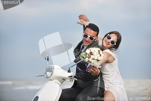 Image of just married couple on the beach ride white scooter