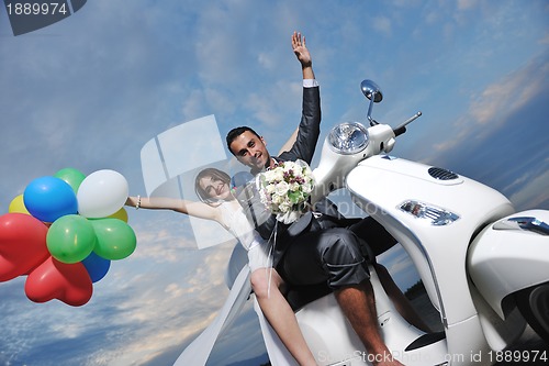 Image of just married couple on the beach ride white scooter