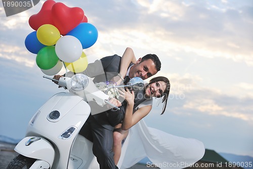 Image of just married couple on the beach ride white scooter