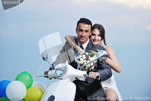 Image of just married couple on the beach ride white scooter