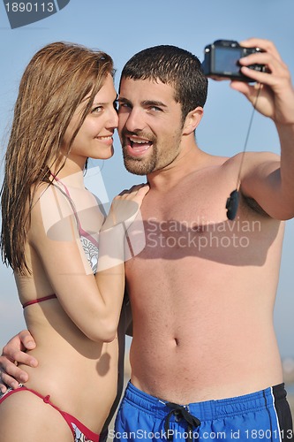Image of happy young couple in love taking photos on beach