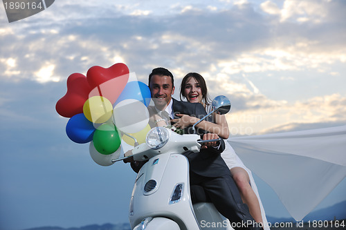 Image of just married couple on the beach ride white scooter