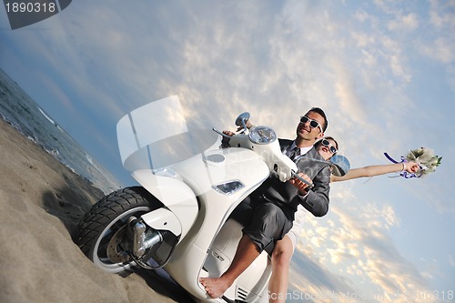 Image of just married couple on the beach ride white scooter