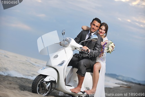 Image of just married couple on the beach ride white scooter