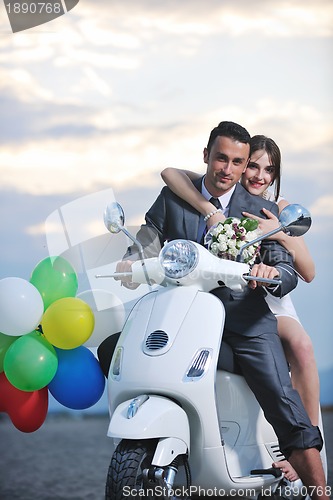 Image of just married couple on the beach ride white scooter