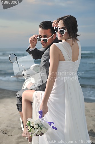 Image of just married couple on the beach ride white scooter