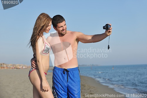 Image of happy young couple in love taking photos on beach