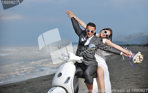 Image of just married couple on the beach ride white scooter