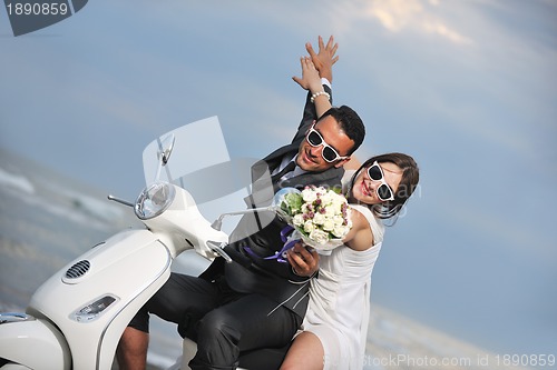 Image of just married couple on the beach ride white scooter