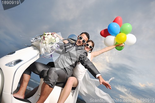 Image of just married couple on the beach ride white scooter