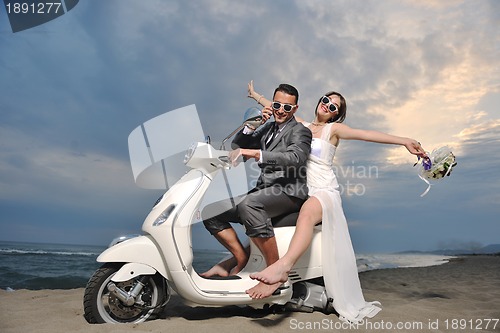 Image of just married couple on the beach ride white scooter