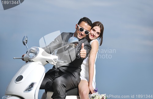 Image of just married couple on the beach ride white scooter