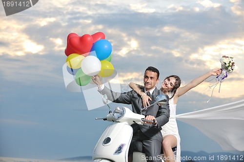 Image of just married couple on the beach ride white scooter