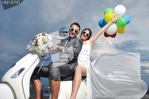 Image of just married couple on the beach ride white scooter