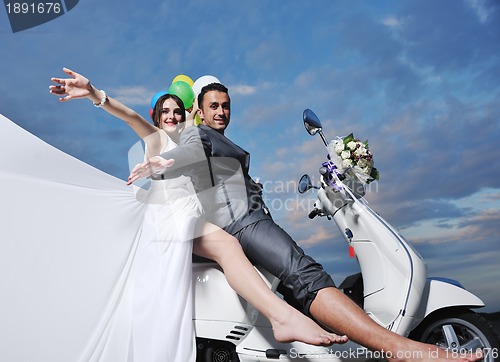 Image of just married couple on the beach ride white scooter