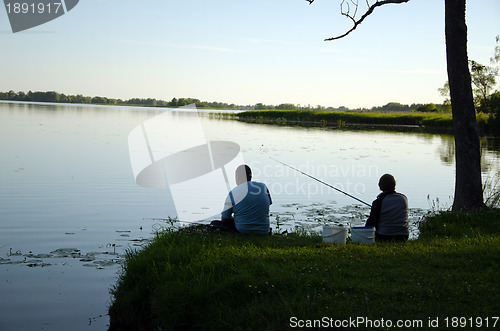 Image of Man and woman sit on lake shore with rods fishing 