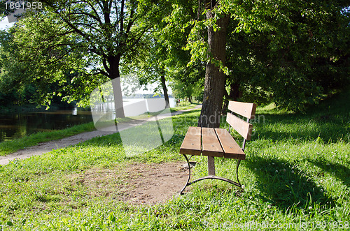 Image of Wooden bench near lake resort. Path between trees 