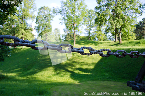 Image of rusty steel chain and green mound blurred 