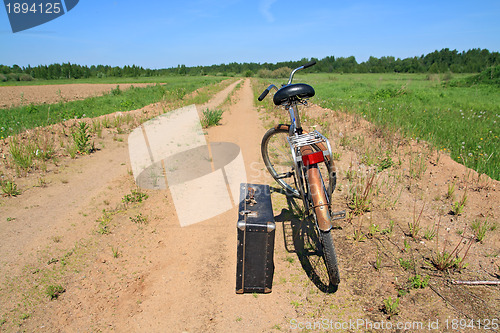 Image of old valise near old bicycle on rural road