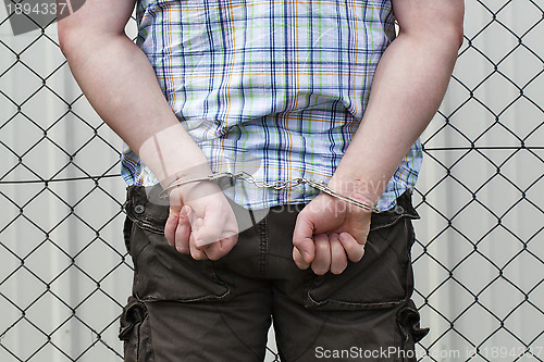 Image of 	Man in handcuffs behind wire fence