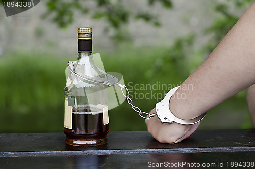 Image of 	Man in handcuffs interconnected with a bottle of alcohol