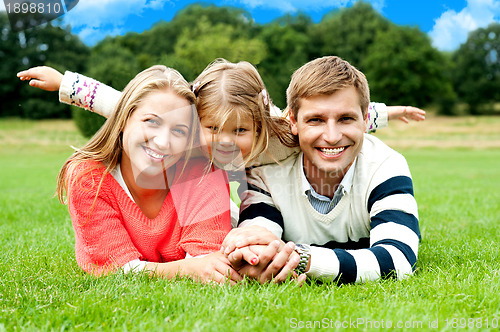 Image of Couple lying in park with their daughter on top